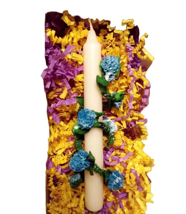A candle with flowers on it is surrounded by purple and yellow paper.