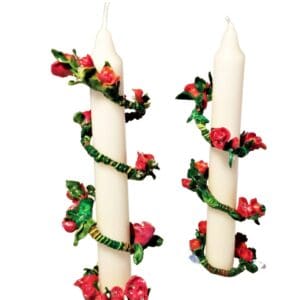 A pair of candles with red flowers and green leaves.