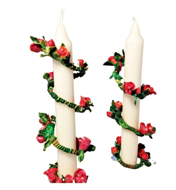A pair of candles with red flowers and green leaves.