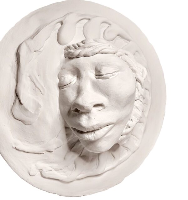 A white sculpture of a face on top of a wall.